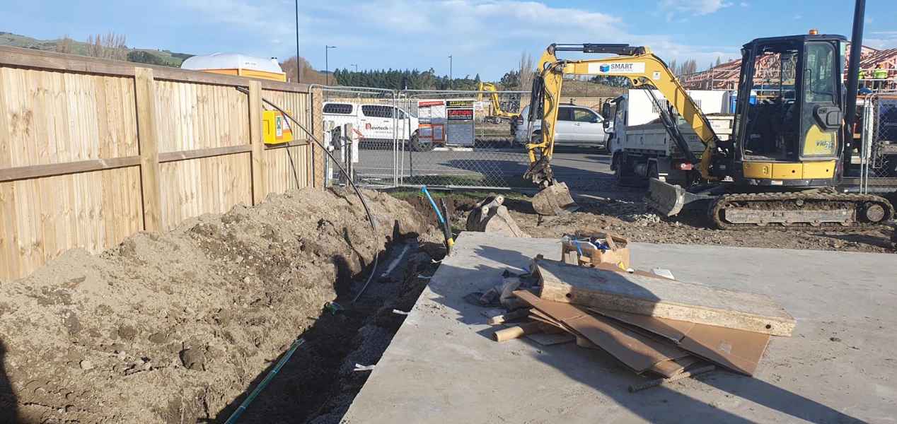Excavated trench with gravel base for construction, featuring PVC pipe and surrounding soil on a building site.